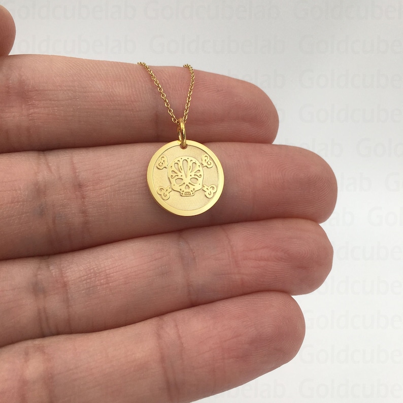 May include: Gold necklace with a round pendant featuring a detailed sugar skull design. The pendant is surrounded by four smaller circles with floral designs.