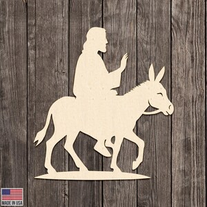 May include: A light-colored wooden cutout depicting a figure riding a donkey. The figure is seated on the donkey, with one arm raised. The donkey is walking to the right. The background is a wooden surface. The words "MADE IN USA" are in the lower left corner.