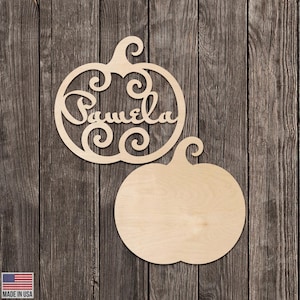 Może przedstawiać: Dwa drewniane wycięcia w kształcie dyni. Jedna dynia ma wycięte imię "Pamela" ozdobną czcionką. Druga dynia ma pełny kształt. Dynie wykonane są z jasnego drewna na tle ciemnego drewna.