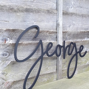 May include: Black wooden name sign with the name "George" written in a cursive script.