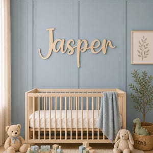 May include: A nursery with a wooden cot, a blue blanket, and a wooden sign spelling "Jasper". The room is decorated with a teddy bear, a stuffed bunny, and a toy train. The wall is painted a light blue, with a framed print.