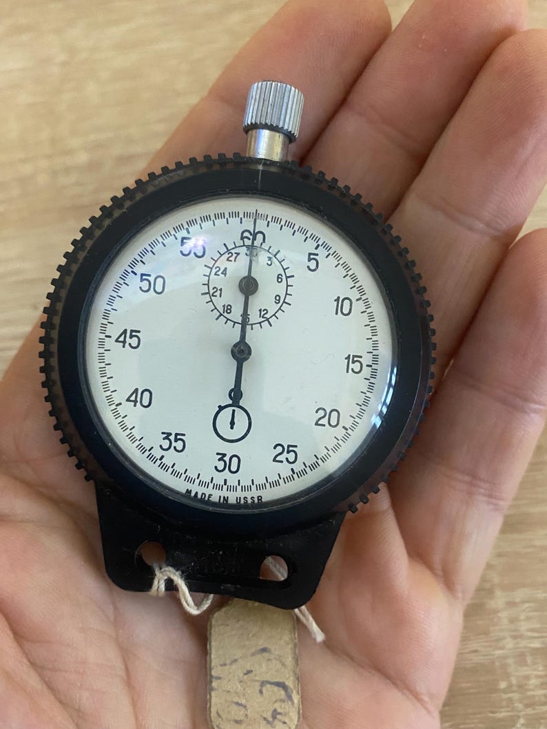 Pu&ograve; includere: Un cronometro vintage con lunetta nera e quadrante bianco con numeri e segni neri. Il cronometro ha una corona argentata e un'impugnatura nera. Il testo "MADE IN USSR" &egrave; visibile sul quadrante.
