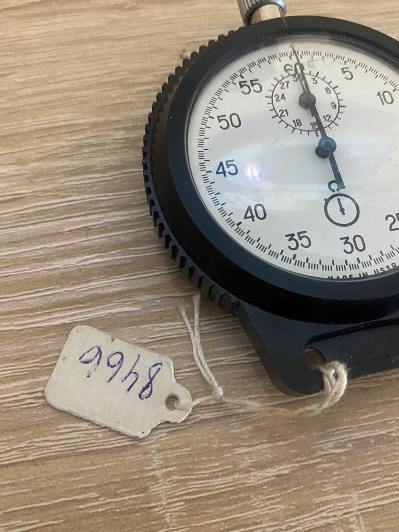 Pu&ograve; includere: Un cronometro nero con quadrante bianco, con numeri e segni neri. Il cronometro ha una lunetta strutturata e una corona di carica. &Egrave; attaccata una piccola etichetta con il numero "8466". Il cronometro &egrave; su una superficie di legno marrone chiaro.