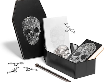 Puede incluir: Una caja de metal negra con forma de ataúd y un diseño de calavera plateada en relieve, que contiene un bloc de notas con estampado de calavera, una pequeña figura de calavera plateada, un cuaderno negro, un bolígrafo metálico y clips con forma de murciélago.