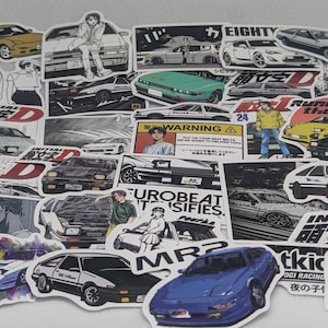 May include: A selection of stickers showcasing car designs, including sports cars and saloons. Some stickers feature Japanese text and anime-style illustrations of people. The stickers are in various colours, including yellow, green, and blue.