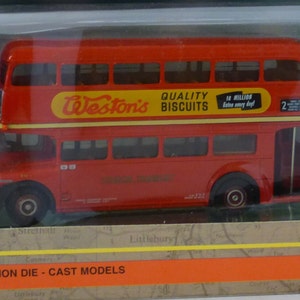 May include: A red double-decker bus model with "Weston's Quality Biscuits" printed on the side. The bus is in a clear plastic display case with a brown and orange cardboard box. The box has "Exclusive First Editions" printed on it.