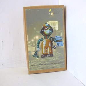 May include: A vintage toy dog illustration on a cardboard backing. The dog is wearing overalls and a hat, holding a bell and a package labeled "EXTRA". The background shows a city scene. Text on the bottom reads "THIS IS NOT A TOY FOR ADULT COLLECTORS ONLY."