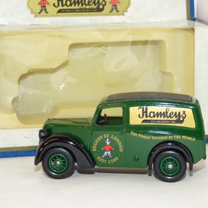 May include: A green Hamleys toy delivery van with black fenders and wheels. The van has the Hamleys logo and text on the side, and the words "Regent St. London EST 1760" are also visible.