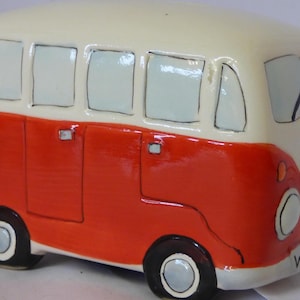 Könnte beinhalten: Ein handbemalter Keramik-Campervan in Rot und Creme. Der Van hat schwarze Räder, Fenster und ein Friedenszeichen auf der Vorderseite. Das Nummernschild lautet WAE196. Ein dekorativer Artikel.