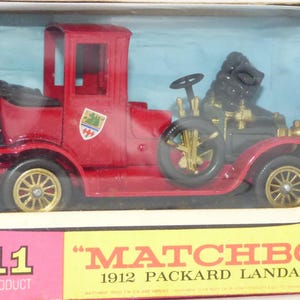 Può includere: Un'auto giocattolo rossa 1912 Packard Landaulet di Matchbox, modello Y-11, nella sua confezione originale. Il veicolo presenta ruote color oro, un'area motore nera e un piccolo stemma sul lato. La scatola riporta il testo Matchbox 1912 Packard Landaulet e Y-11 A Lesney Product.