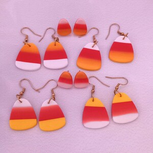 Puede incluir: Un conjunto de seis pares de pendientes de maíz dulce. Los pendientes están hechos de arcilla polimérica y están pintados en los colores del maíz dulce: amarillo, naranja y blanco. Los pendientes están unidos a ganchos de color dorado.