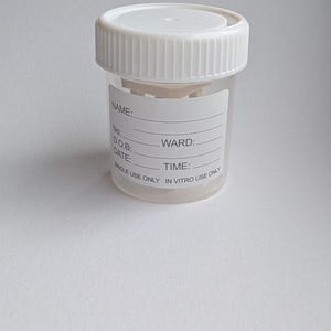 Peut inclure: Un r&eacute;cipient transparent en plastique pour &eacute;chantillons avec un couvercle &agrave; vis blanc. Le r&eacute;cipient comporte une &eacute;tiquette avec des espaces pour les informations du patient, dont "NOM:" et "SERVICE:." Le texte "SINGLE USE ONLY IN VITRO USE ONLY" est imprim&eacute;.