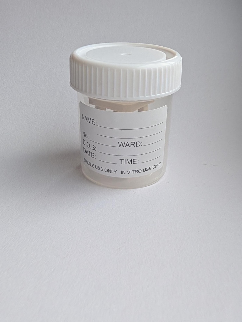 Peut inclure: Un r&eacute;cipient transparent en plastique pour &eacute;chantillons avec un couvercle &agrave; vis blanc. Le r&eacute;cipient comporte une &eacute;tiquette avec des espaces pour les informations du patient, dont "NOM:" et "SERVICE:." Le texte "SINGLE USE ONLY IN VITRO USE ONLY" est imprim&eacute;.