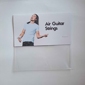 Op de afbeelding: Een witte kaart met de tekst "Air Guitar Strings" en een foto van een persoon die luchtgitarre speelt.