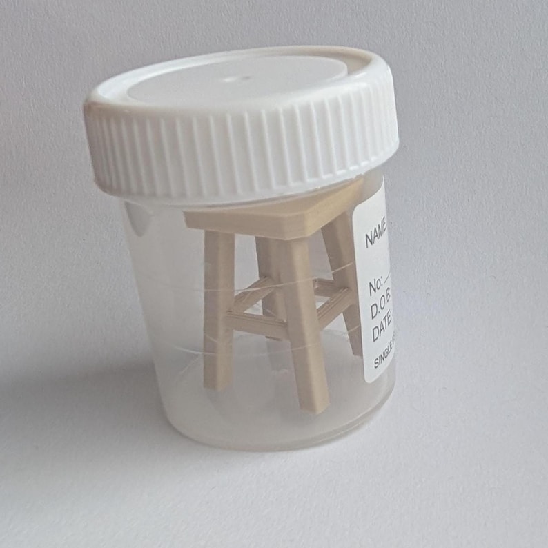 Peut inclure: Un petit tabouret en bois &agrave; l'int&eacute;rieur d'un r&eacute;cipient en plastique transparent avec un couvercle blanc. Le r&eacute;cipient porte une &eacute;tiquette avec du texte. Le tabouret est brun clair et a quatre pieds.