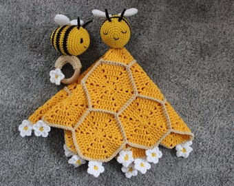 May include: A handmade crochet baby blanket in a honeycomb pattern, featuring two adorable bee-shaped toys. The blanket is yellow with a beige border and white daisy accents. One bee toy has a wooden ring with a flower.