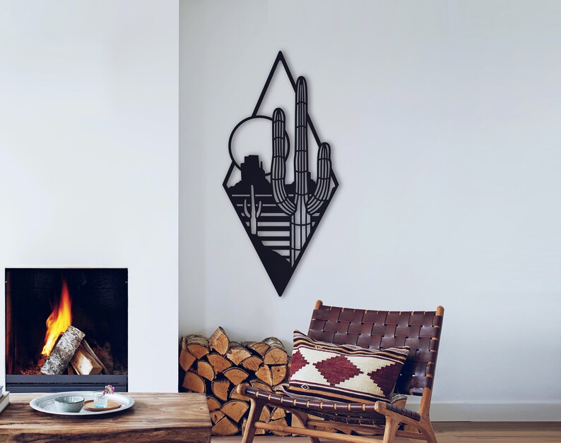 May include: Black metal wall art in the shape of a diamond featuring a silhouette of a desert landscape with a cactus, mountains, and a sun.