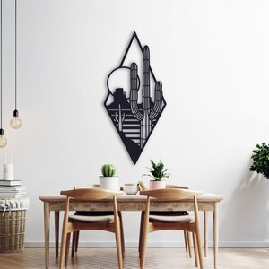 May include: Black metal wall art featuring a geometric diamond shape with a silhouette of a desert landscape, including a cactus, mountains, and a sun.