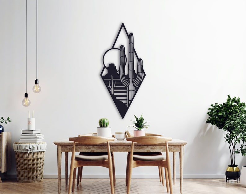 May include: Black metal wall art featuring a geometric diamond shape with a silhouette of a desert landscape, including a cactus, mountains, and a sun.