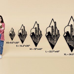 May include: Five sizes of black metal wall art depicting a desert landscape with cacti and mountains. The sizes are XS: 9.5 inches by 20 inches, S: 14.2 inches by 30 inches, M: 19 inches by 40 inches, L: 22.7 inches by 48 inches, and XL: 26.5 inches by 56 inches.