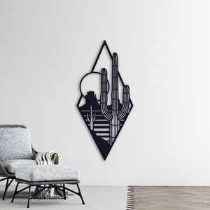 May include: Black metal wall art featuring a geometric diamond shape with a desert landscape silhouette inside. The design includes a cactus, mountains, and a sun.