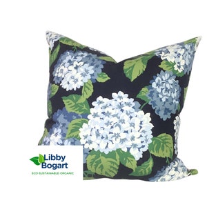 May include: A navy blue cushion with a floral pattern of white and blue hydrangeas and green leaves. The cushion has the text "Libby Bogart ECO-SUSTAINABLE-ORGANIC" printed on the bottom left corner.