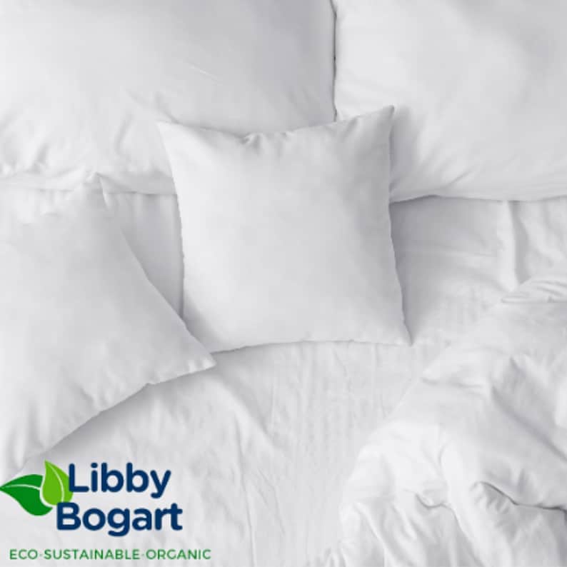 K&ouml;nnte beinhalten: Draufsicht auf ein Bett mit wei&szlig;er Bettw&auml;sche, einschlie&szlig;lich Kissen und einer Bettdecke. Die Kissen sind quadratisch und flauschig, und die Laken sind glatt. Das Bild enth&auml;lt das Libby Bogart-Logo mit dem Text "ECO-SUSTAINABLE-ORGANIC".