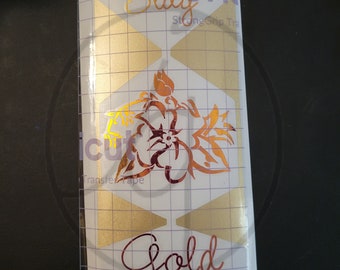 May include: Gold vinyl decal with a hibiscus flower design on a clear transfer sheet. The decal is labelled "Stay Cricut Strong Grip Transfer Tape" and "Gold".