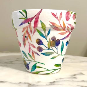 May include: A white ceramic flower pot with a watercolor floral design featuring pink, green, blue, and orange leaves and berries.