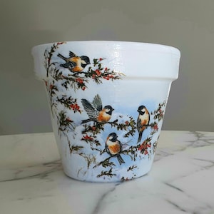 Könnte beinhalten: Weißer Keramiktopf mit einem Wintermotiv mit vier Vögeln und roten Beeren. Der Topf hat einen blau-weißen Hintergrund mit Schneeeffekt.