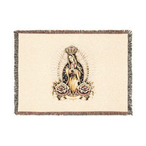May include: Cream-colored woven throw blanket featuring an illustration of a religious figure with a crown, surrounded by a halo and two roses. The blanket has a fringed border in shades of brown and black.