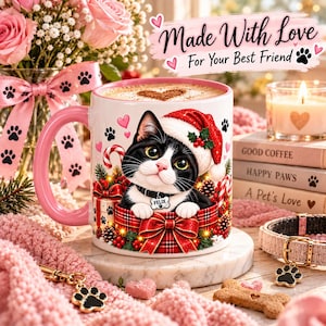 Puede incluir: Una taza de cerámica blanca con un gato blanco y negro que lleva un gorro de Papá Noel, sentado dentro de una caja de regalo con un lazo de cuadros rojos. La taza muestra el nombre Felix en una placa de collar, rodeado de bastones de caramelo.