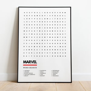 May include: A black and white word search puzzle with the word "MARVEL" in red at the top. The puzzle features characters and locations from the Marvel Cinematic Universe. The word search is framed in a black frame and is sitting on a light wood floor.