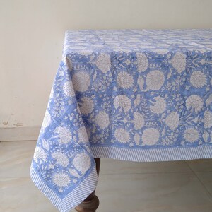 May include: A blue and white floral tablecloth with a striped border. The tablecloth is draped over a wooden table with turned legs.