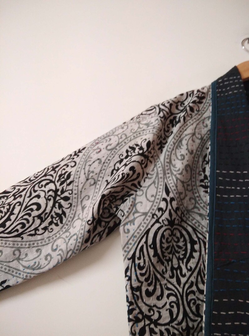 K&ouml;nnte beinhalten: Ein lang&auml;rmeliges Kleidungsst&uuml;ck mit einem schwarzen und wei&szlig;en Paisley-Muster auf dem &Auml;rmel und einem dunkelblauen und schwarzen gemusterten Stoff auf der Vorderseite. Das Kleidungsst&uuml;ck ist gefaltet und h&auml;ngt an einem Kleiderb&uuml;gel.