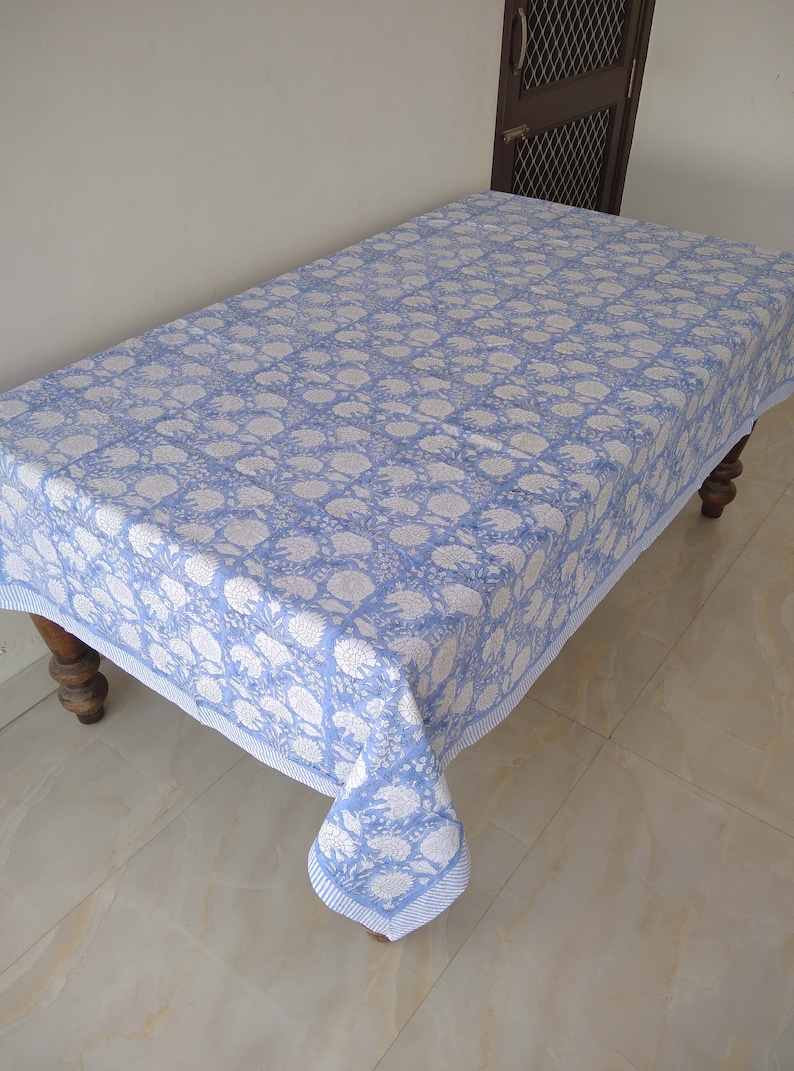 May include: A light blue tablecloth with a white floral pattern. The tablecloth is rectangular and has a white border.