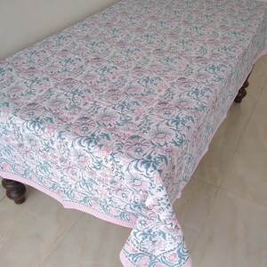 Peut inclure: Une nappe blanche avec un motif floral rose et turquoise. La nappe a une bordure ray&eacute;e rose et blanche.