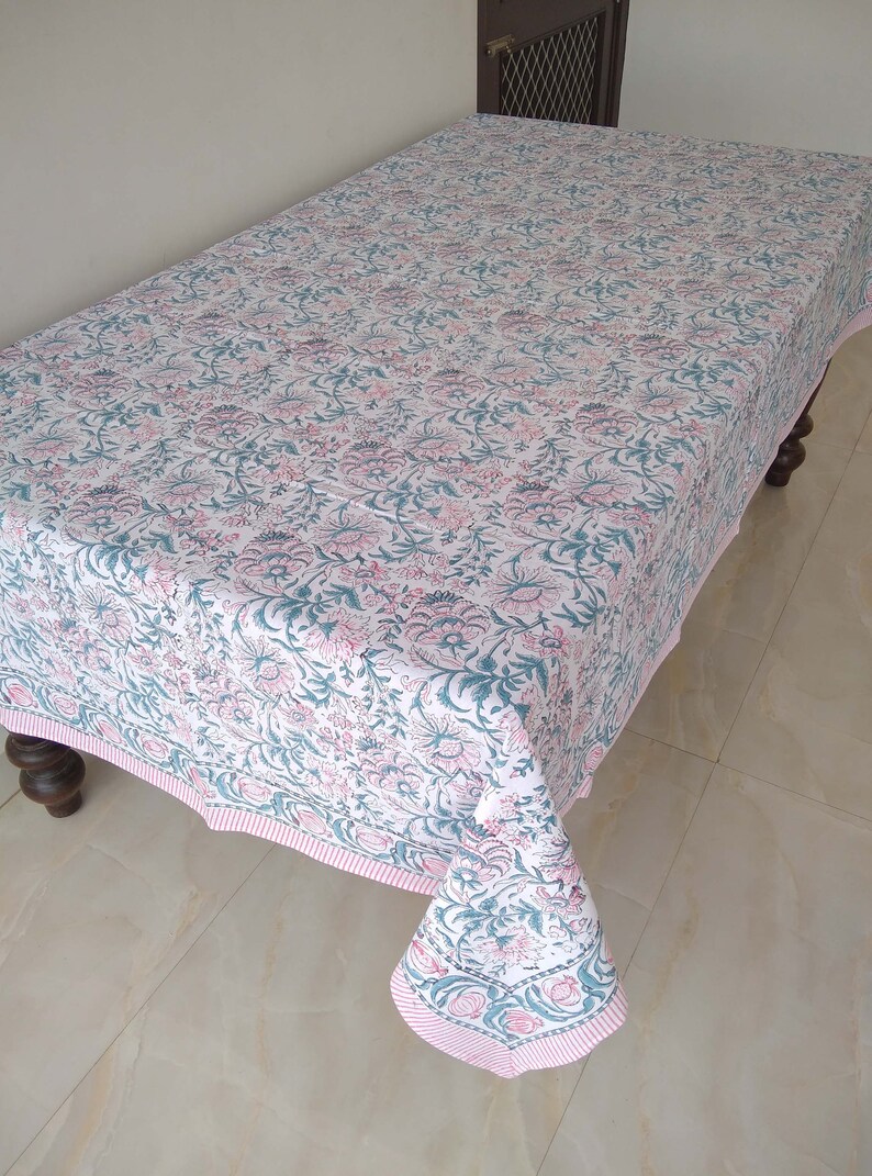 Peut inclure: Une nappe blanche avec un motif floral rose et turquoise. La nappe a une bordure ray&eacute;e rose et blanche.