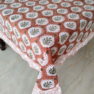Pu&ograve; includere: Una tovaglia color terracotta con un motivo floreale bianco e verde. La tovaglia ha un bordo a festoni ed &egrave; realizzata in cotone.