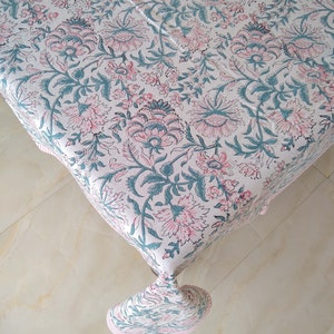 Peut inclure: Une nappe blanche avec un motif floral dans les tons rose et turquoise. La nappe a un bord frang&eacute; et est en coton.