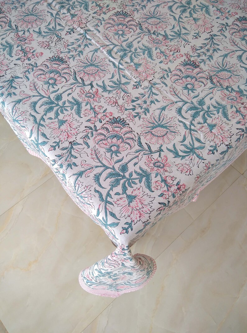 Peut inclure: Une nappe blanche avec un motif floral dans les tons rose et turquoise. La nappe a un bord frang&eacute; et est en coton.