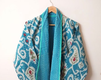 Könnte beinhalten: Eine türkisblaue gesteppte Jacke mit einem weißen und blauen Paisley-Muster. Die Jacke hat einen grünen Besatz und einen Schalkragen.