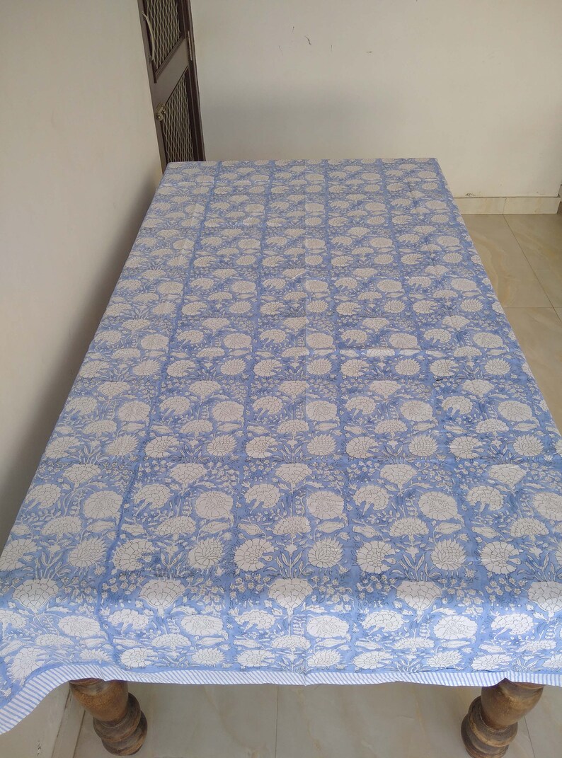 May include: A blue and white floral tablecloth with a striped border. The tablecloth is made of cotton and is perfect for a dining table.