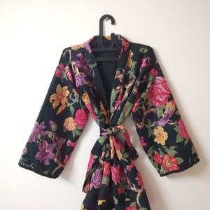 May include: A black floral print kimono robe with a tie belt. The robe features a variety of colorful flowers and birds on a black background.