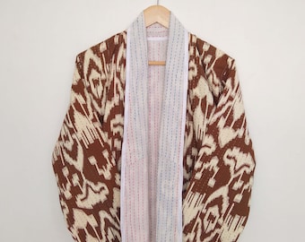 Könnte beinhalten: Eine gesteppte Jacke mit braunem und weißem Muster, weißem Kragen und weißem Besatz. Die Jacke ist offen und hängt an einem Kleiderbügel.