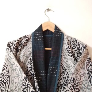 K&ouml;nnte beinhalten: Ein Kimono mit schwarz-wei&szlig;em Muster, einem dunkelblauen und schwarzen Kragen und Besatz. Der Kimono h&auml;ngt an einem Holzb&uuml;gel.
