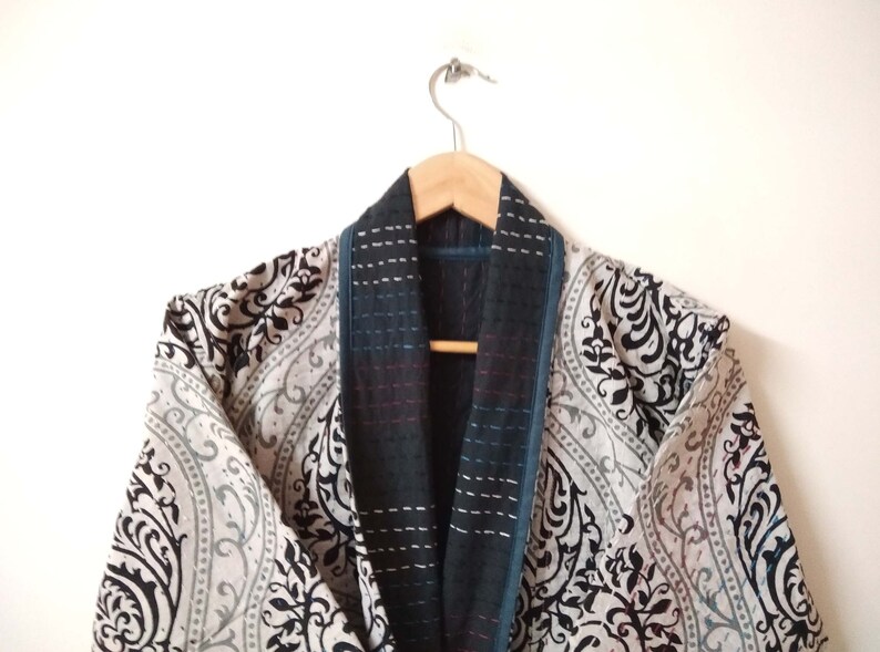 K&ouml;nnte beinhalten: Ein Kimono mit schwarz-wei&szlig;em Muster, einem dunkelblauen und schwarzen Kragen und Besatz. Der Kimono h&auml;ngt an einem Holzb&uuml;gel.