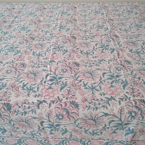 Peut inclure: Une nappe blanche avec un motif floral dans les tons rose et turquoise. La nappe a une bordure avec un motif r&eacute;p&eacute;t&eacute; de rose et de turquoise.