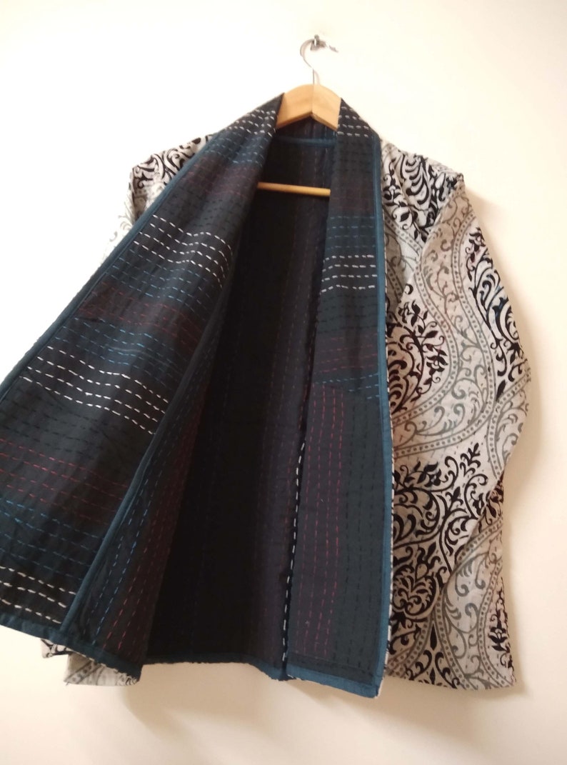 K&ouml;nnte beinhalten: Eine Jacke mit schwarz-wei&szlig;em Muster und tealfarbener Innenfutter. Die Jacke ist offen und h&auml;ngt an einem Holzb&uuml;gel.