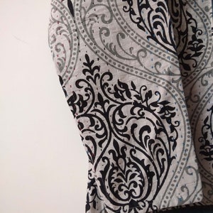 K&ouml;nnte beinhalten: Nahaufnahme eines grauen und schwarzen Stoffes mit Paisley-Muster. Der Stoff hat eine gesteppte Textur und ist umgeklappt.